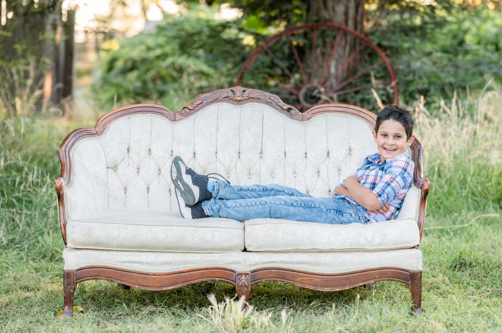 Little boy seated on a couch in a field in family photo session at West 12 Ranch with Gia Chong Photography, Lodi CA photographer