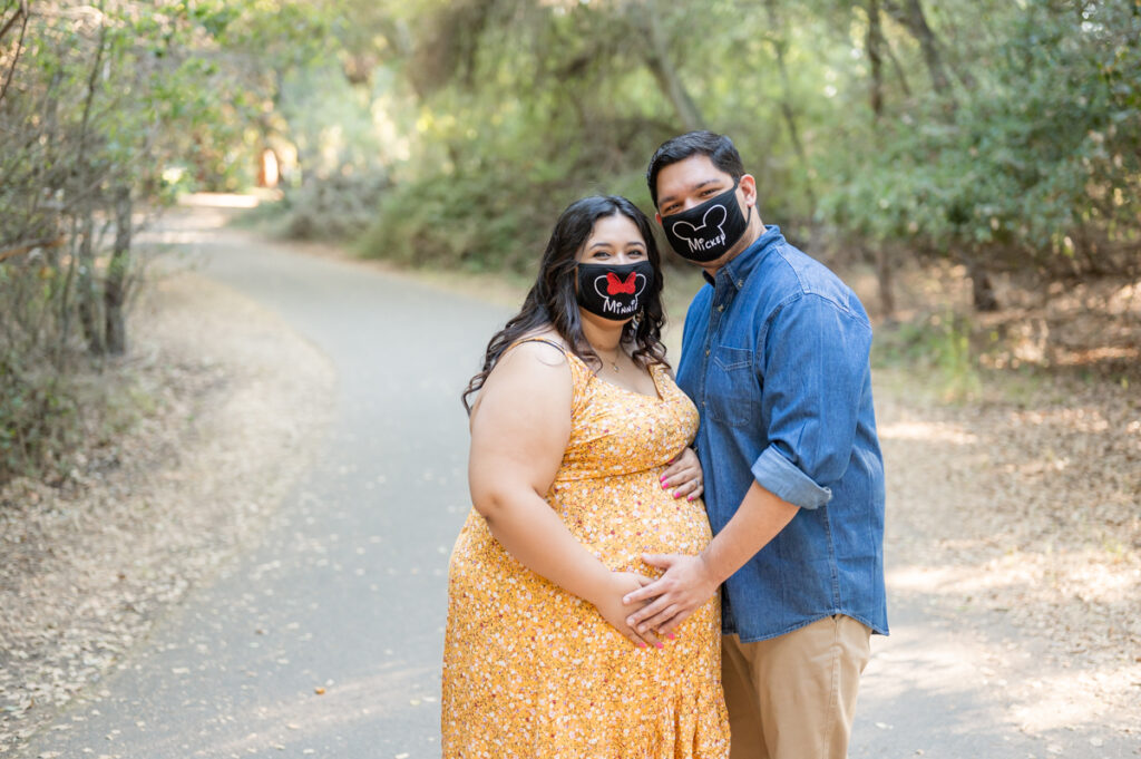 Dad and pregnant mom with Disney masks posing on a nature trail during a maternity session at Lodi Lake Park, Lodi CA with Gia Chong Photography, Lodi Photographer