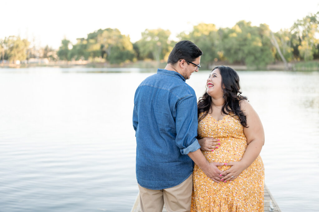 Dad and pregnant mom posing on a dock near the water during a maternity session at Lodi Lake Park, Lodi CA with Gia Chong Photography, Lodi Photographer
