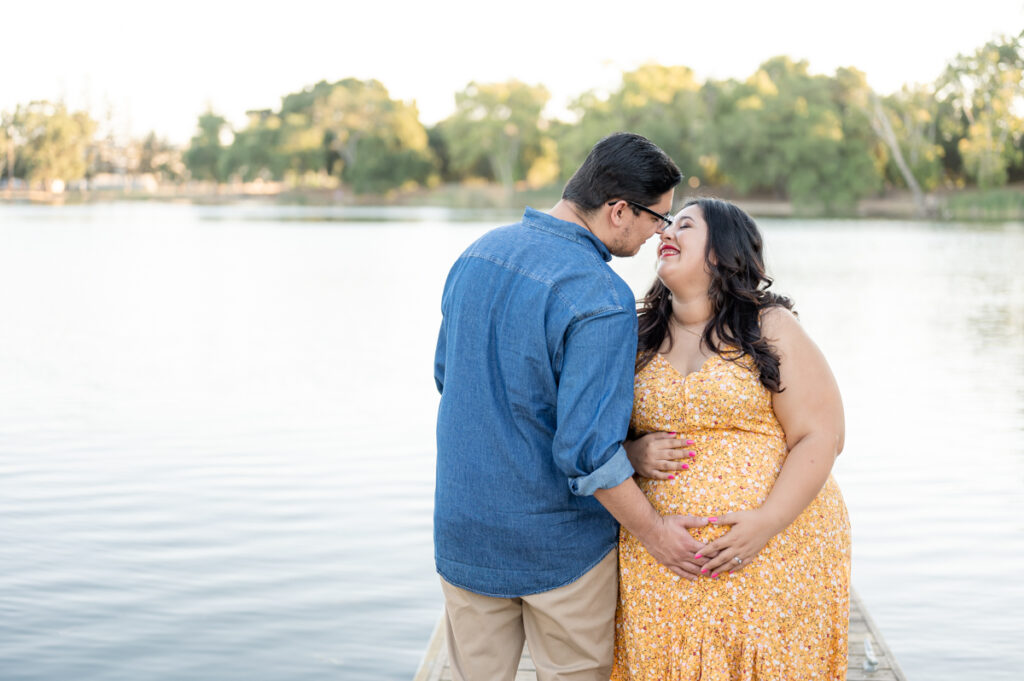 Parents kissing on a dock near the water during a maternity session at Lodi Lake Park, Lodi CA with Gia Chong Photography, Lodi Photographer