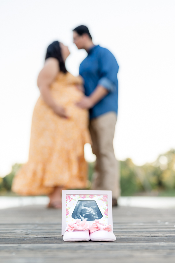 An Ultrasound photo and baby shoes dock near the water during a maternity session at Lodi Lake Park, Lodi CA with Gia Chong Photography, Lodi Photographer