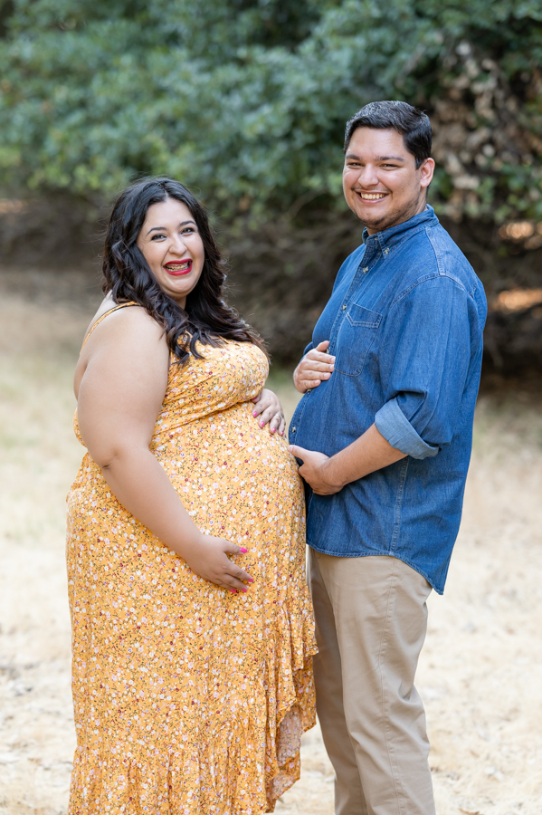 Dad and pregnant mom posing with their bellies in a field during a maternity session at Lodi Lake Park, Lodi CA with Gia Chong Photography, Lodi Photographer