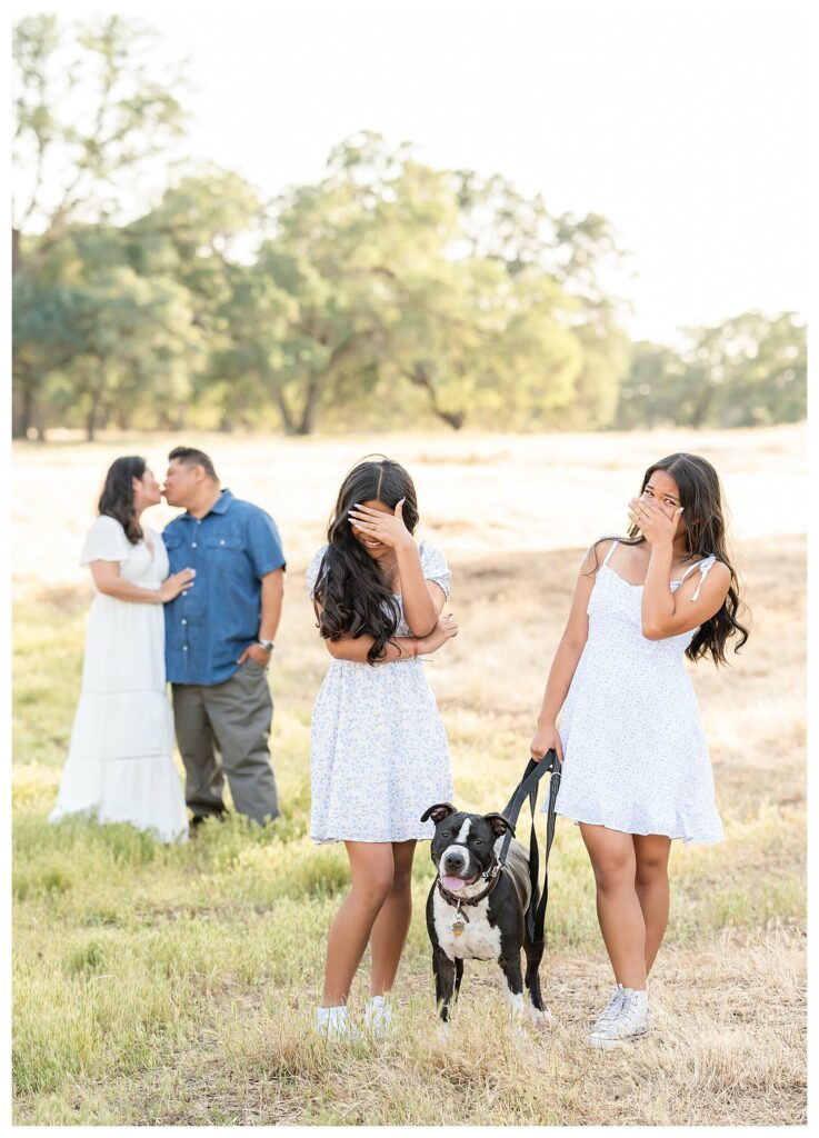 parents kissing in the background and daughters are embarrassed during outdoor family photo session Roseville CA