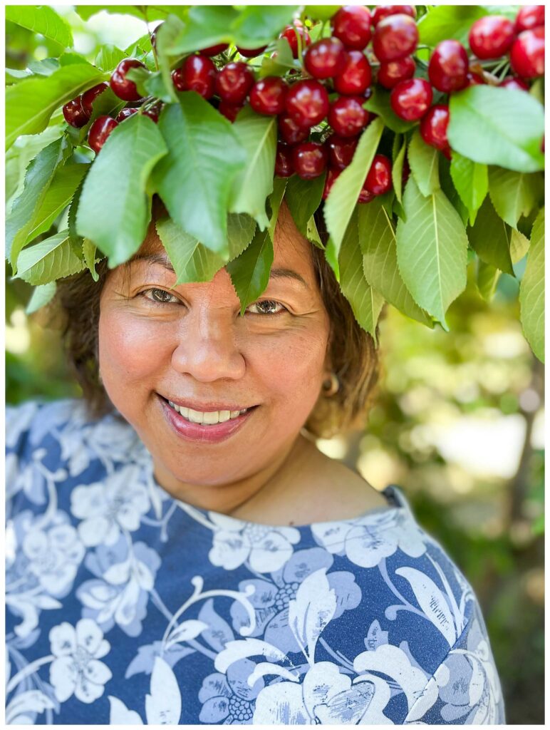 woman smiling at the camera in a cherry orchard