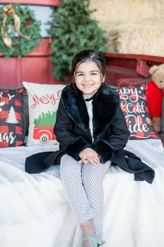 little girl smiling at the camera while seated on a red truck