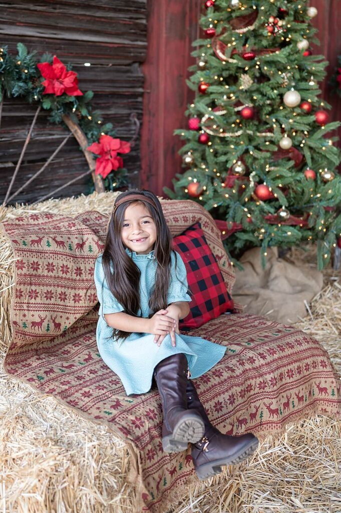 Little girl seated and smiling at a Christmas set up at West 12 Ranch Lodi CA