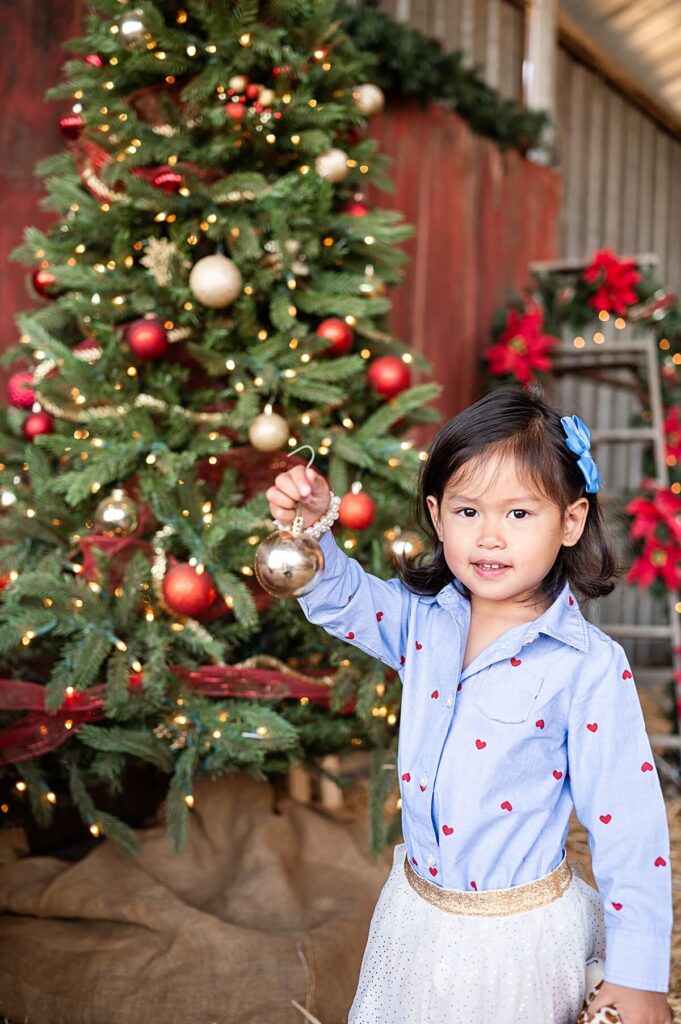 Little girl smiling and holding a Christmas ornament during a family session at West 12 Ranch Lodi