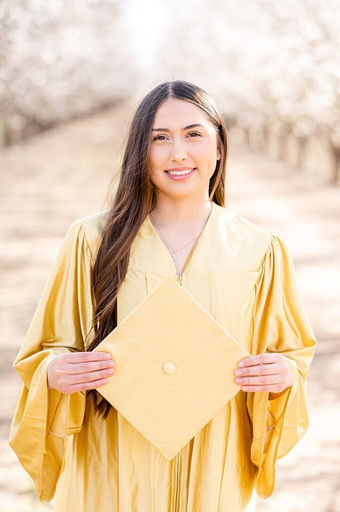 senior girl holding her grad cap and smiling during her almond blossom grad shoot