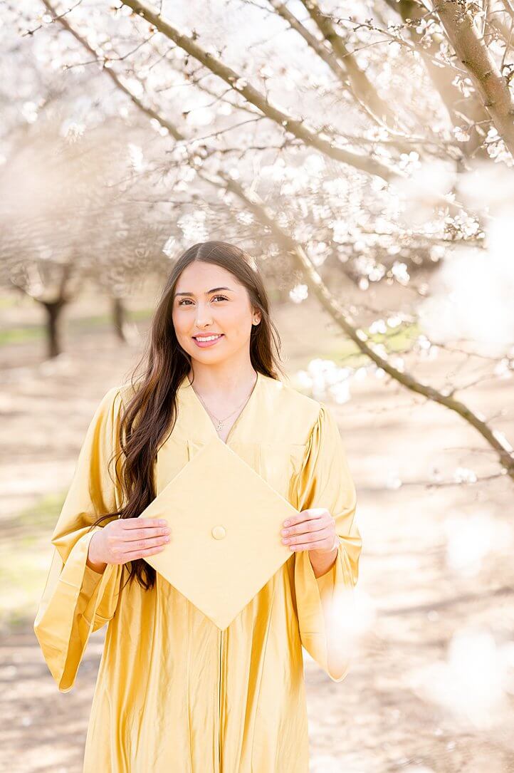 Senior girl holding her grad cap and smiling during her almond blossom grad session