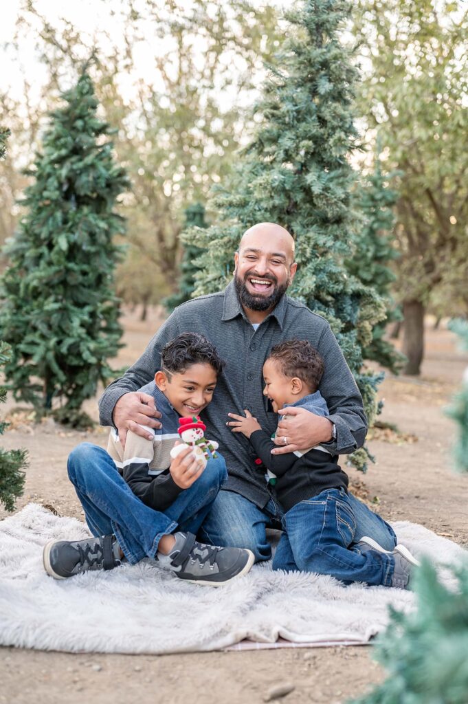 Dad and sons seated on a blanket and laughing curing their family session in Stockton CA