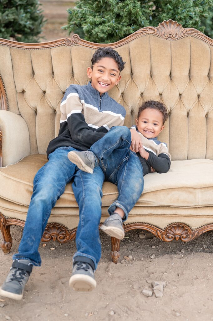 Young boys smiling at the camera while sitting on a couch during their Christmas Tree Farm Photo Session