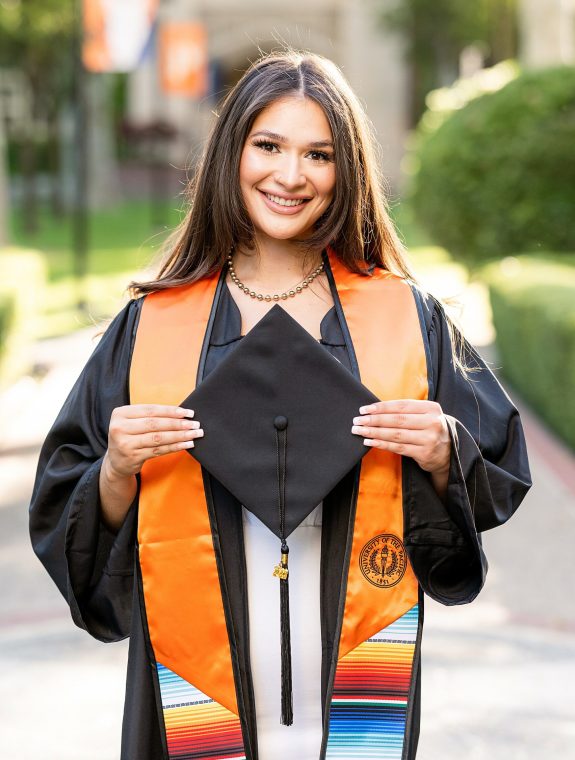 College grad holding her cap and smiling at the camera